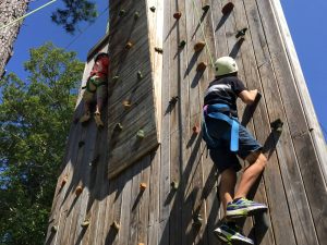 Youngsters conquer a climbing wall at a challenge course at Tall Timbers Conference Center.